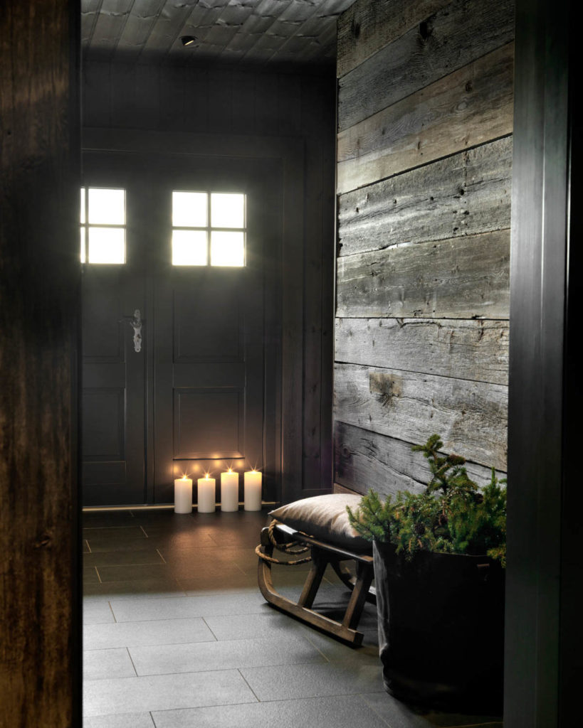 Dark doors in the entrance area of a cabin. Gray slate flooring and large, rustic wooden planks on the wall.