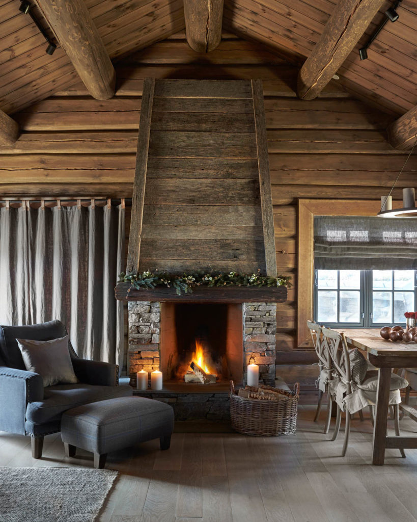 Large living room in a cabin with armchair and dining table in front of fireplace in stone and wood