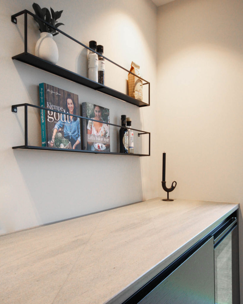 A kitchen countertop in natural stone of light Oppdal quartzite slate. On the wall above hang shelves with cookbooks.