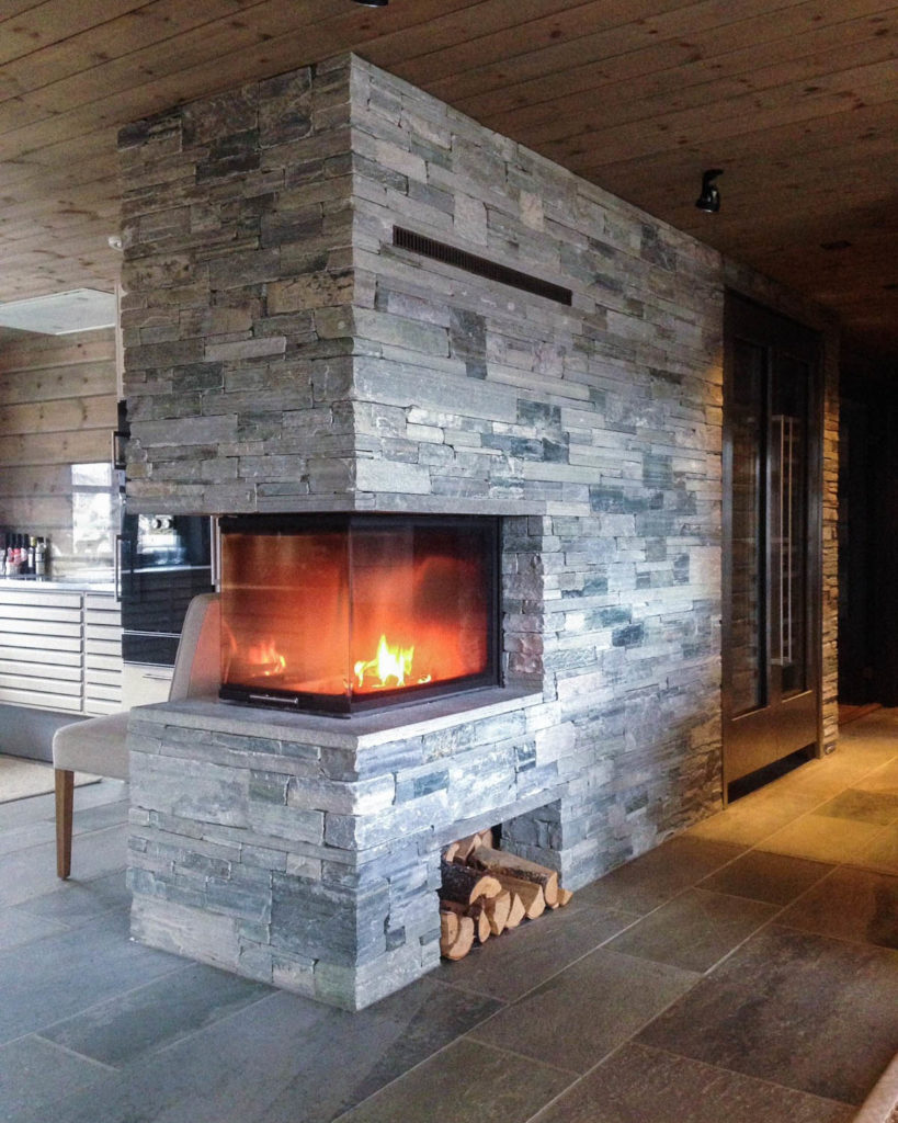 Cabin fireplace of Light Oppdal slate bricks that is a room divider between kitchen and living room. Slate tiles on the floor of the same natural stone.
