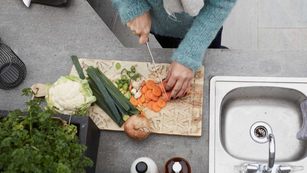 A lady cuts root vegetables in an outdoor kitchen that has a natural stone countertop (antique-brushed Oppdal slate).