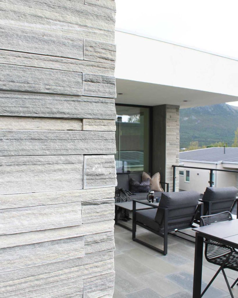 Detail of the corner of a slate facade where slate bricks of light Oppdal quartzite are embedded in each other. The terrace in the background has a deck of slate tiles.