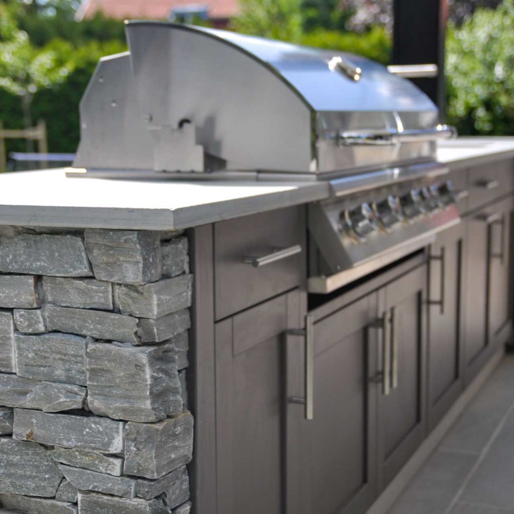 Outdoor kitchen with Oppdal quartzite slate bricks and tiles on the ground. The outdoor grill has cabinets and drawers and a large grill with a stainless steel hood.