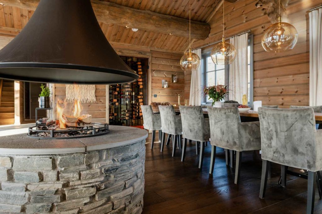 Round fireplace of wallbricks in slate, centered in the room with dining table in the background. The wallbricks and copings are Oppdal quartzite slate