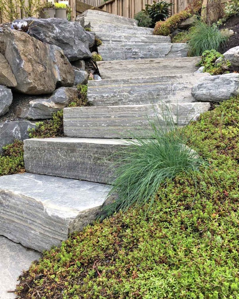 A close-up of a staircase of natural stone with lush planting on the side. The steps are solid slate in Oppdal quartzite from Norway.