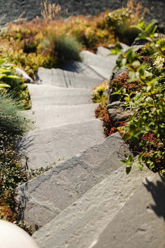 A slate staircase on a slope with lush vegetation on the sides of the natural stone staircase.