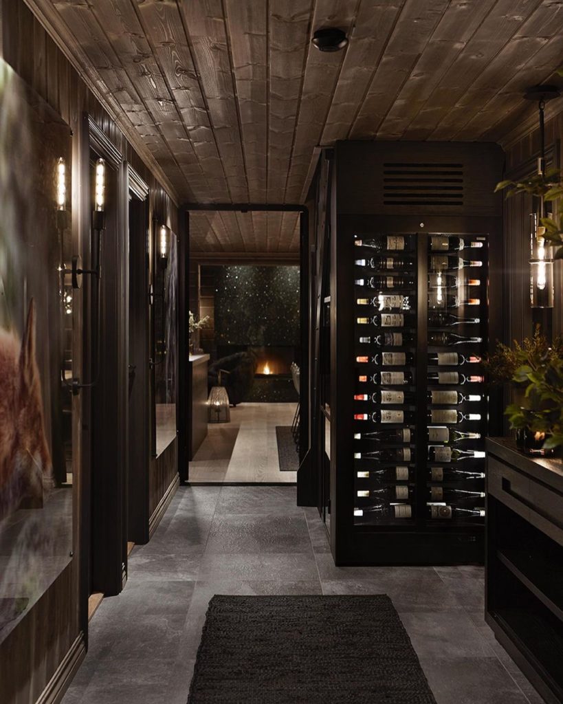 En herskaplig entrè på en hytte med grå skiferflis. I gangen står et stort vinskap med glassdører. 