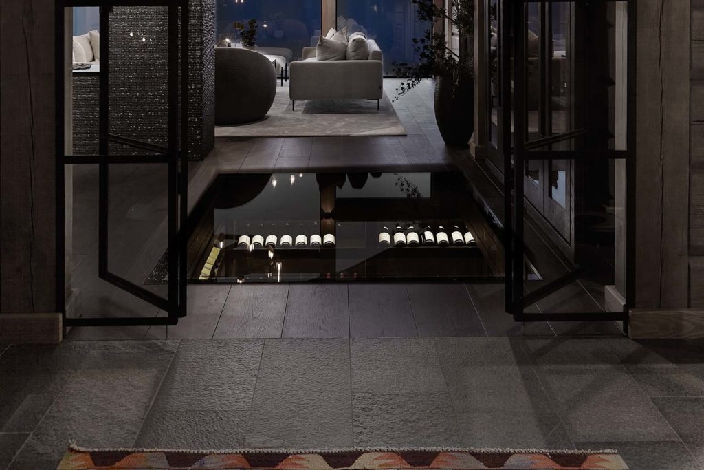 En vacker timmerstuga med grått kakel i skiffer på golvet i hallen i kombination med mörk parkett med infälld glaspanel.