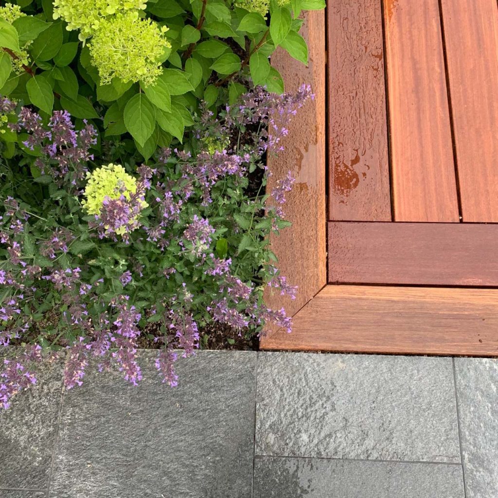 A detailed picture of outdoor tiles of Offerdal slate together with golden wood and green plants.