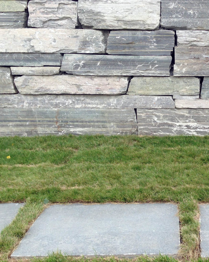Light gray stepping stones laid in grass in front of a dry wall of slate bricks. All the slate is Oppdal quartzite.