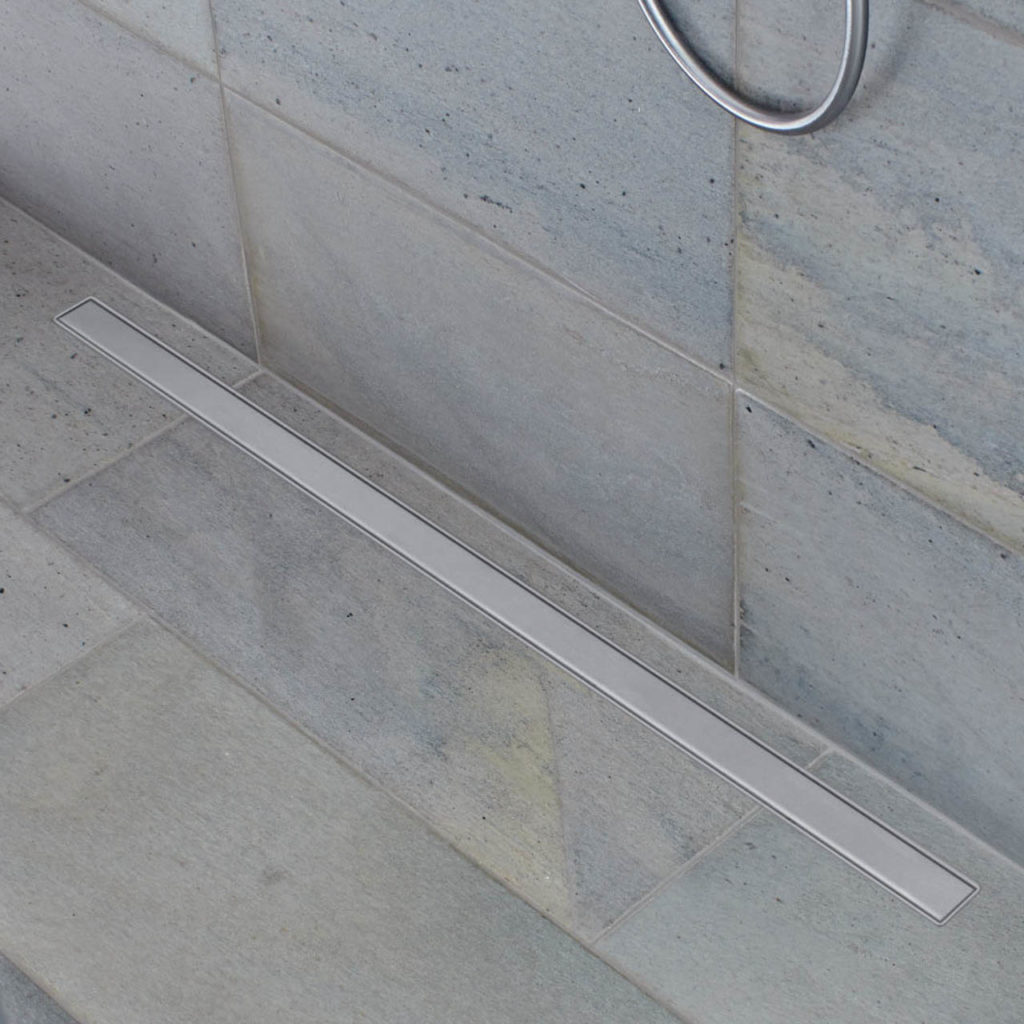 Details of a shower with light gray slate tiles on the floor and wall. A long drain is embedded in the slate tiles.