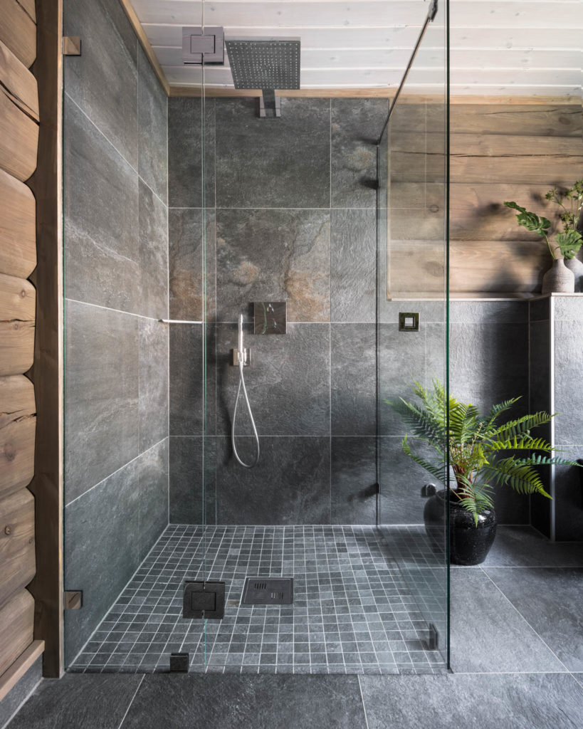 Cabin bathroom with gray slate tiles, rustic timber walls and green planting.
