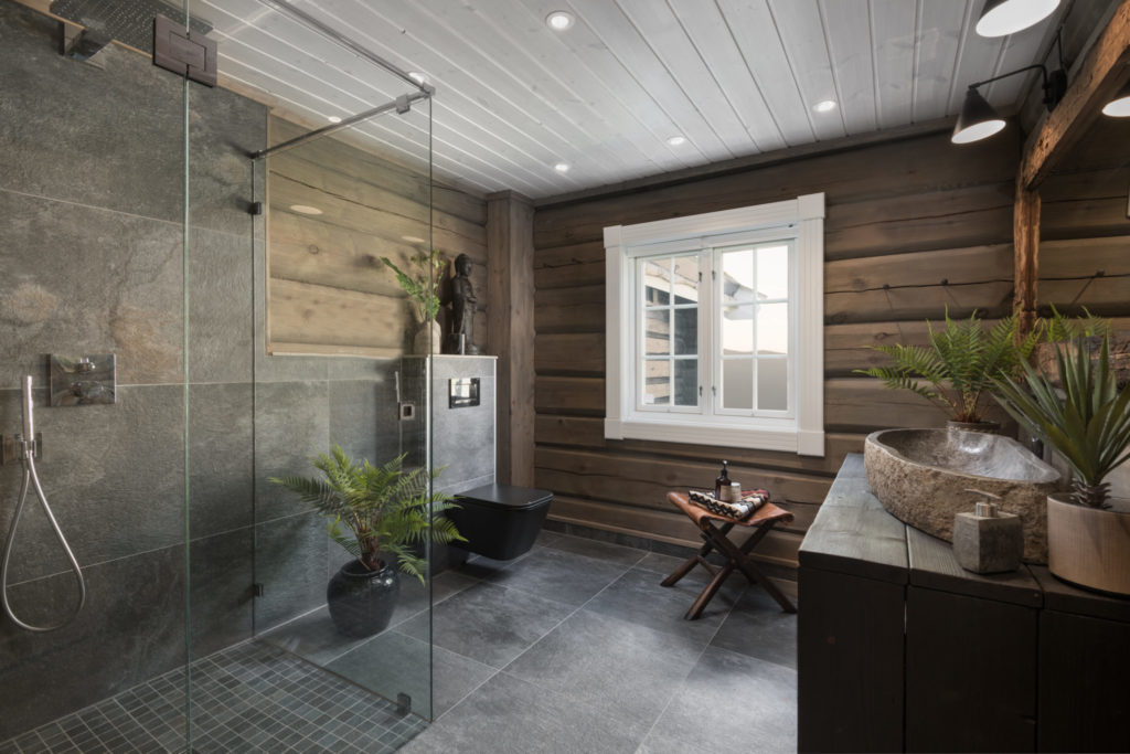 Cabin bathroom with large slate tiles, timber walls, dark interior and green plantings. 