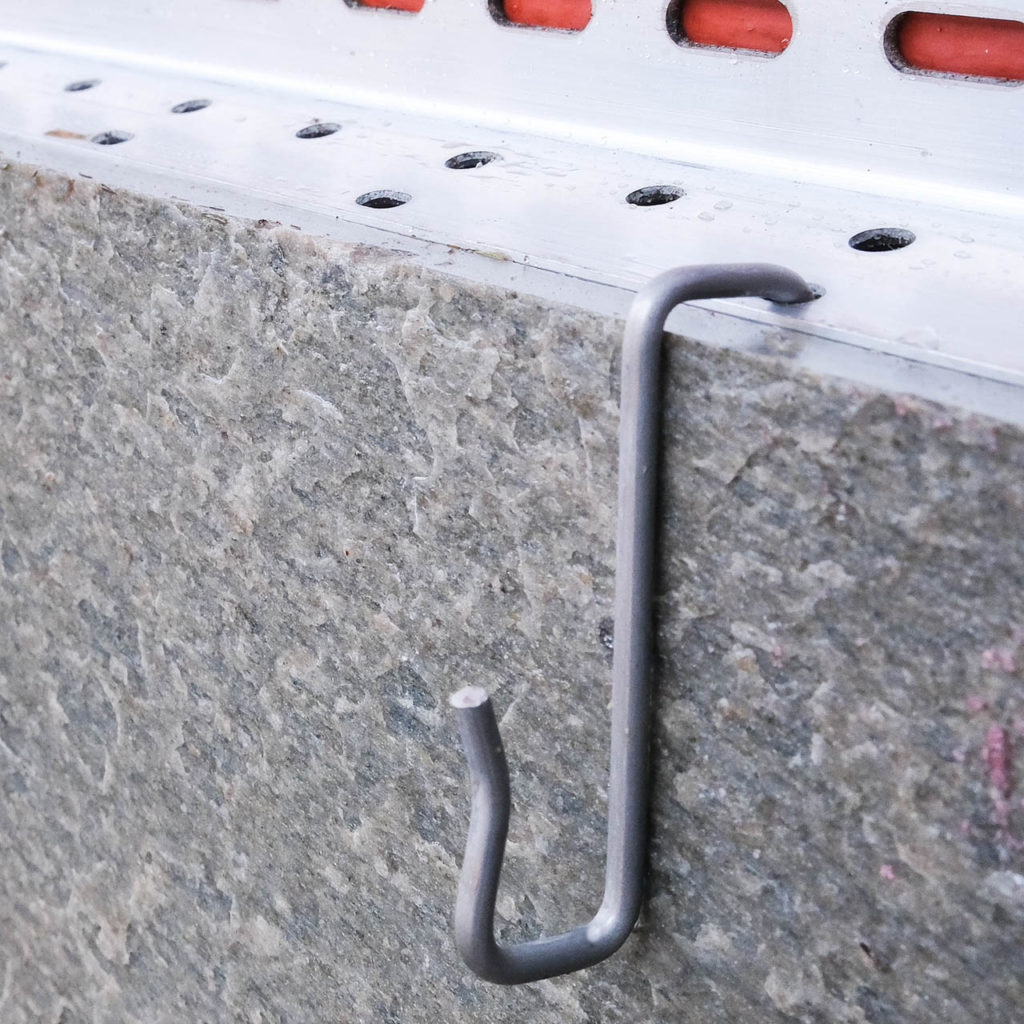 Close-up of an facade installation system for thin slate slabs  with aluminum rails and hooks.