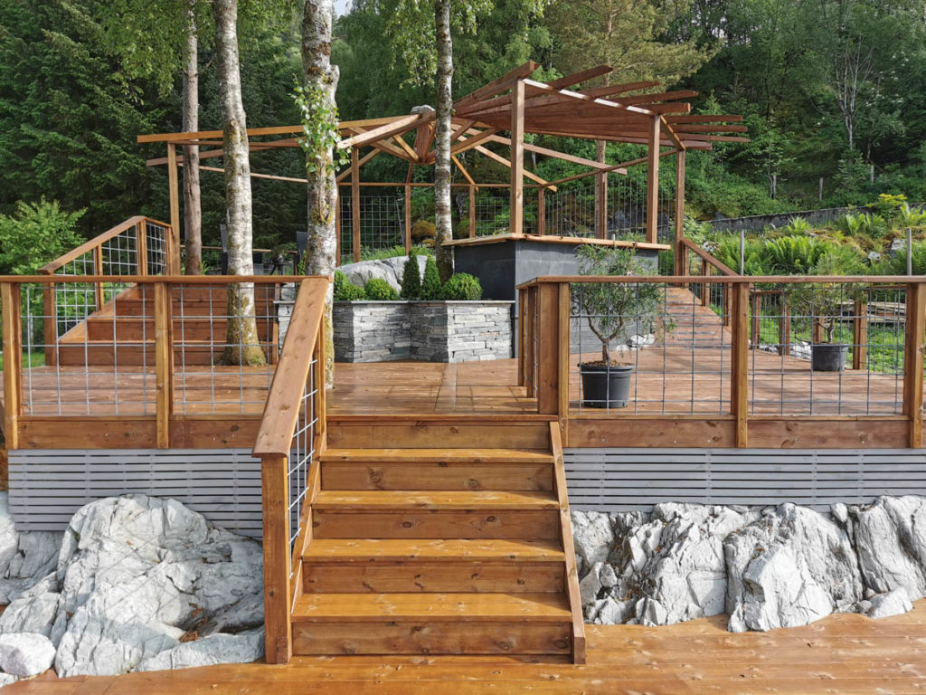 A wooden staircase up to a large terrace with a pavilion and with slate flower beds built as a drywall.