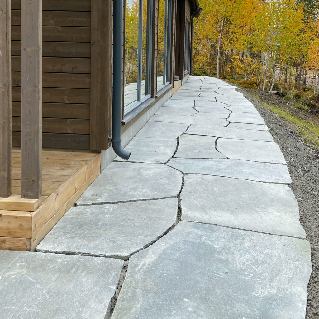 A wide footpath of slate that goes around a cabin.
