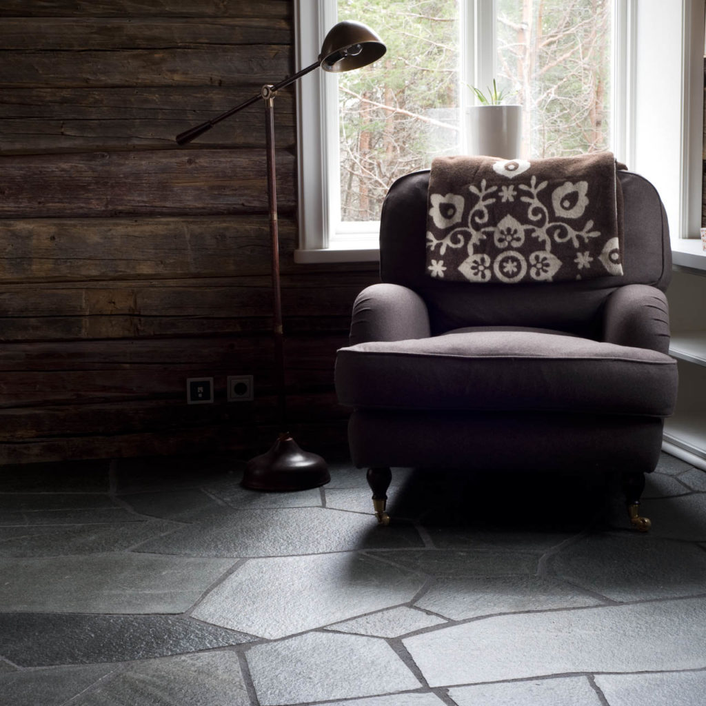 A cabin with dark timber walls and a large armchair. On the floor is gray crazy paving of Offerdal slate.
