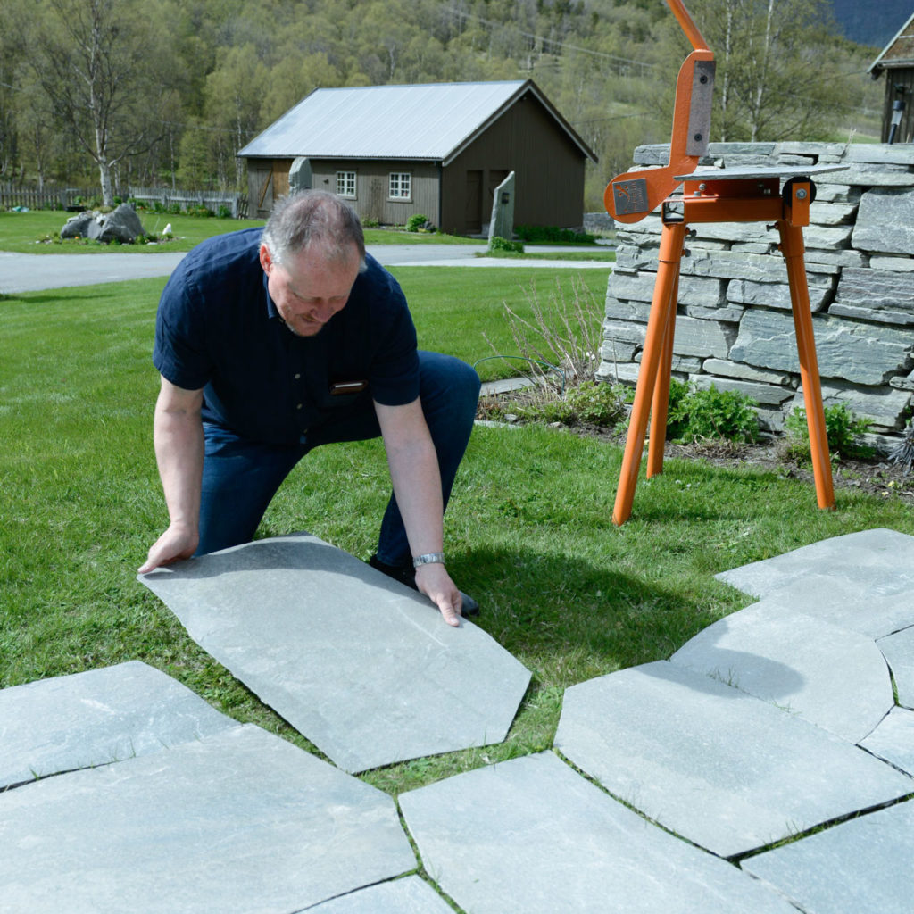 A flagstone is shaped with a slate scissors and laid down in place among the other slabs.