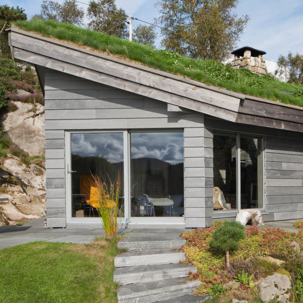 Moderne hytte med fasadeskifer og store vindusflater. En skifertrapp går ned til hagen.