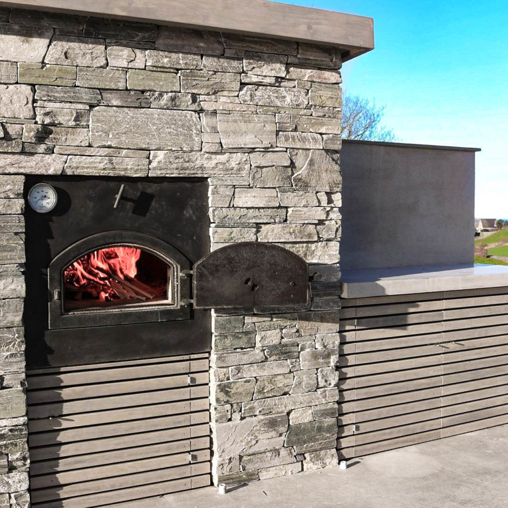 En terrasse med en pizzaovn integrert i en tørrmur av lys Oppdalskifer murstein. 