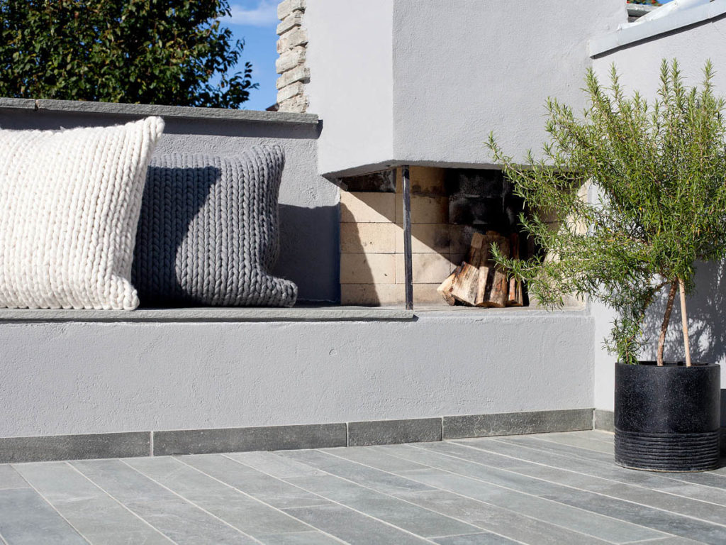 A terrace with outdoor fireplace and bench with pillows. Narrow slate tiles are glued to the cast slab.