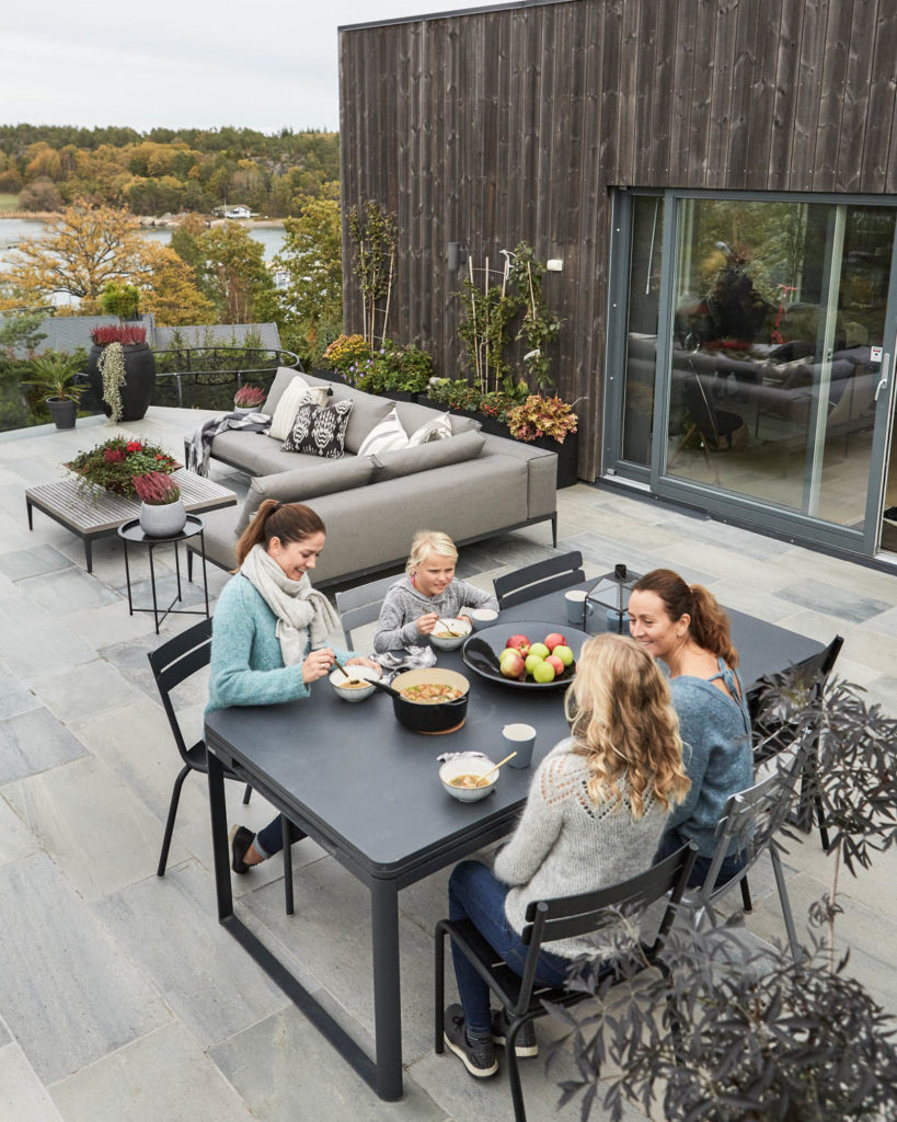 A large terrace with light gray outdoor tiles of Oppdal slate. A family is sitting and eating.