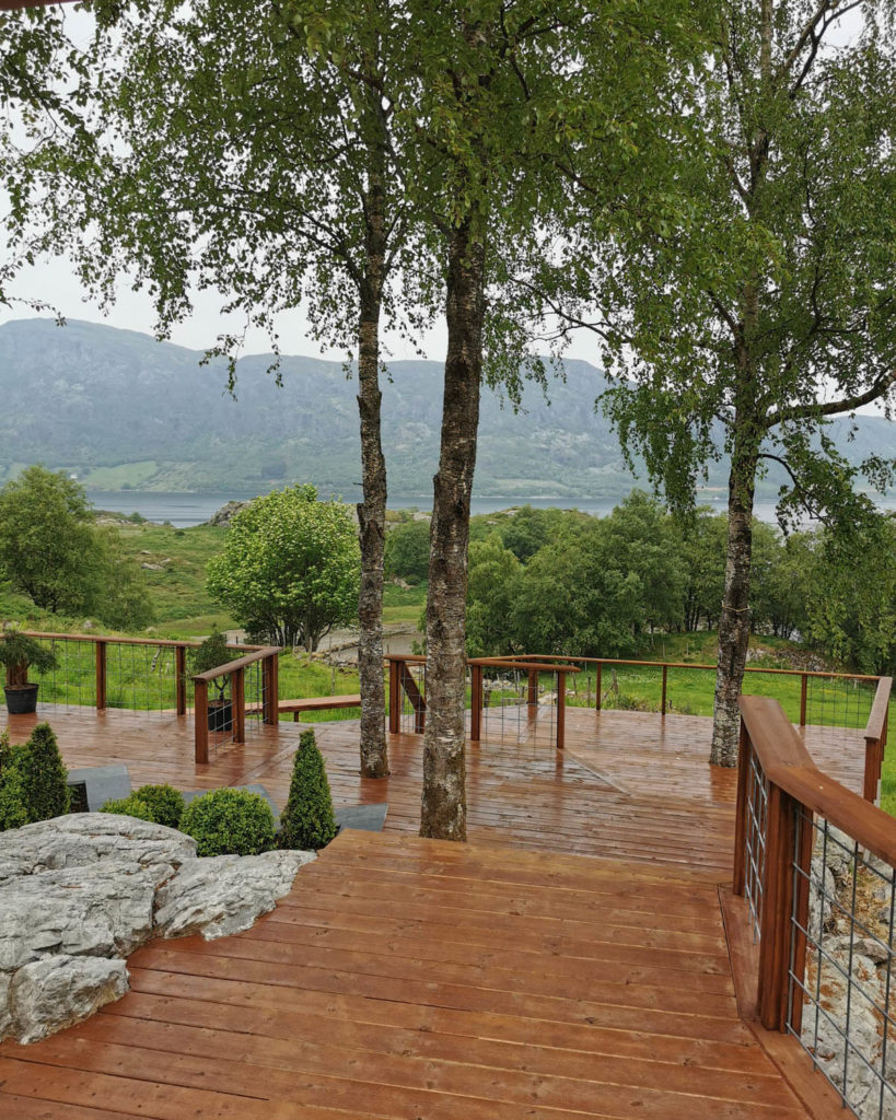 En stor terrasse som er bygd over flere plan midt i naturen og med vakker utsikt mot et vann.