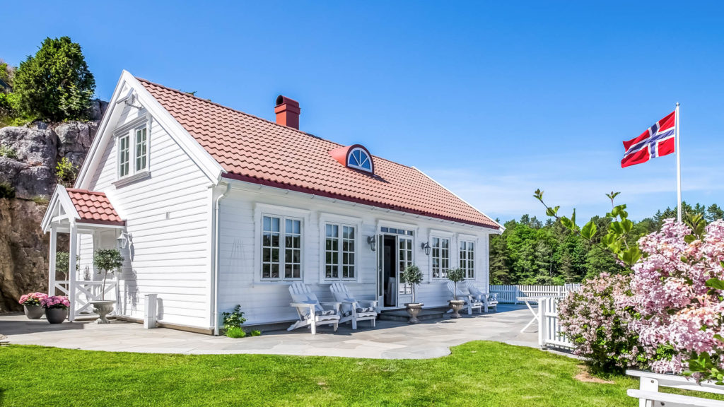 Et hvitt hus med en flott uteplass belagt med bruddskifer  fra Oppdal. Et norsk flagg vaier i vinden.