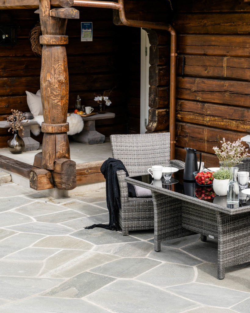 A cabin terrace with outdoor furniture and a covered coffee table. Light Oppdal flagstones have been laid on the ground.