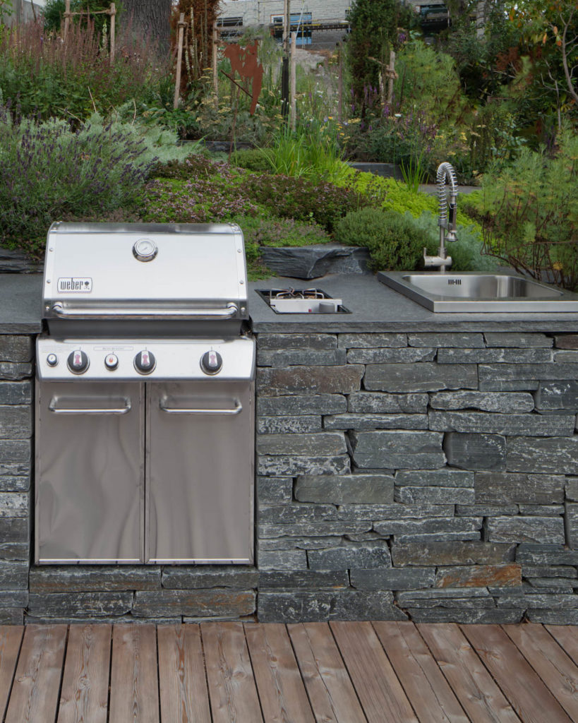 A stainless steel grill and outdoor kitchen integrated in a beautiful dry wall of Offerdal slate.