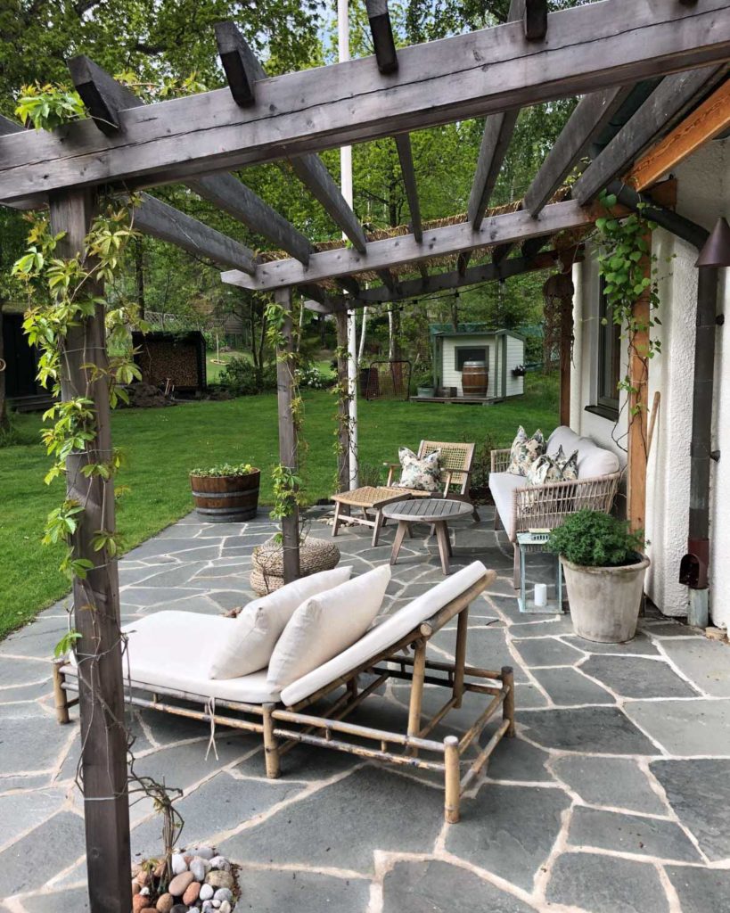 A terrace with pergola and crazy paving of Offerdal slate. A bamboo sun lounger and sitting area stand on the patio.