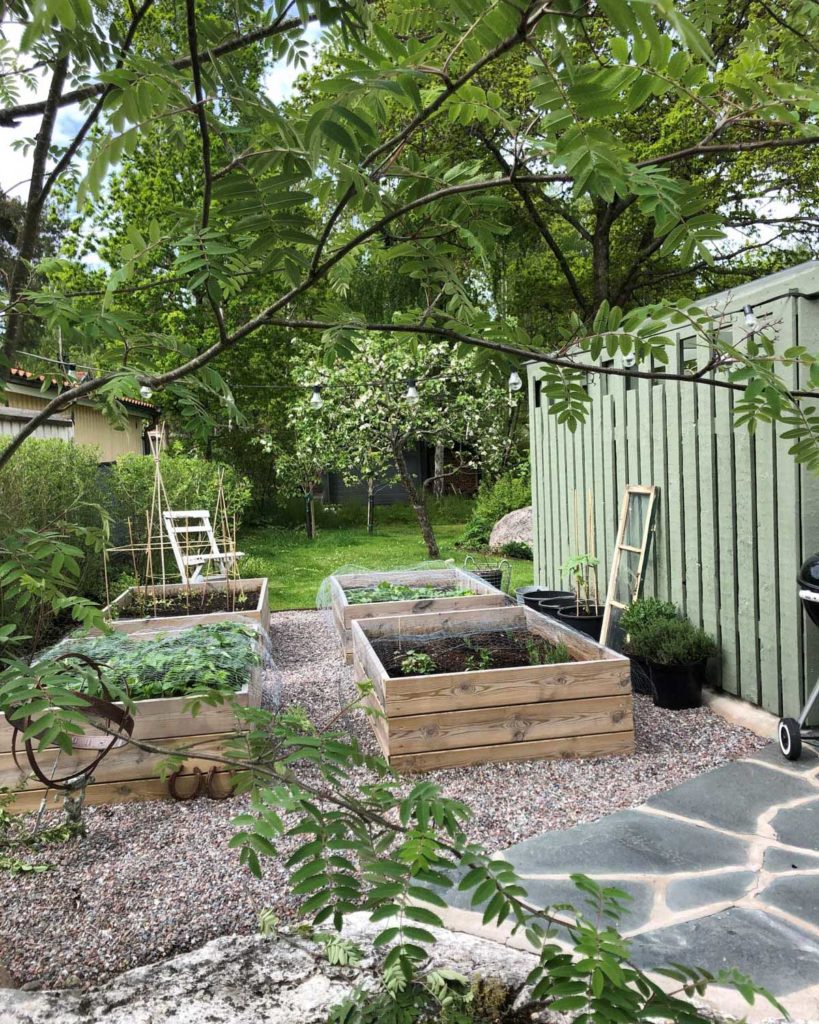 En trädgård med planteringskärl för grönsaker intill en terrass av Offerdal trädgårdsskiffer.