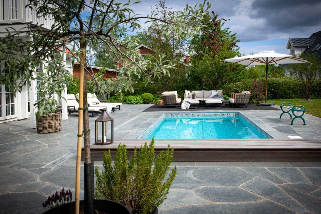 A large paved terrace with swimming pool, sun loungers and seating area. The crazy paving of Offerdal slate is dark gray.