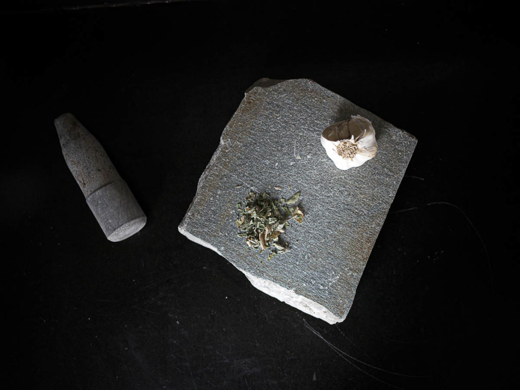 A thick slate slab used as a mortar. At the top lies herbs and garlic.