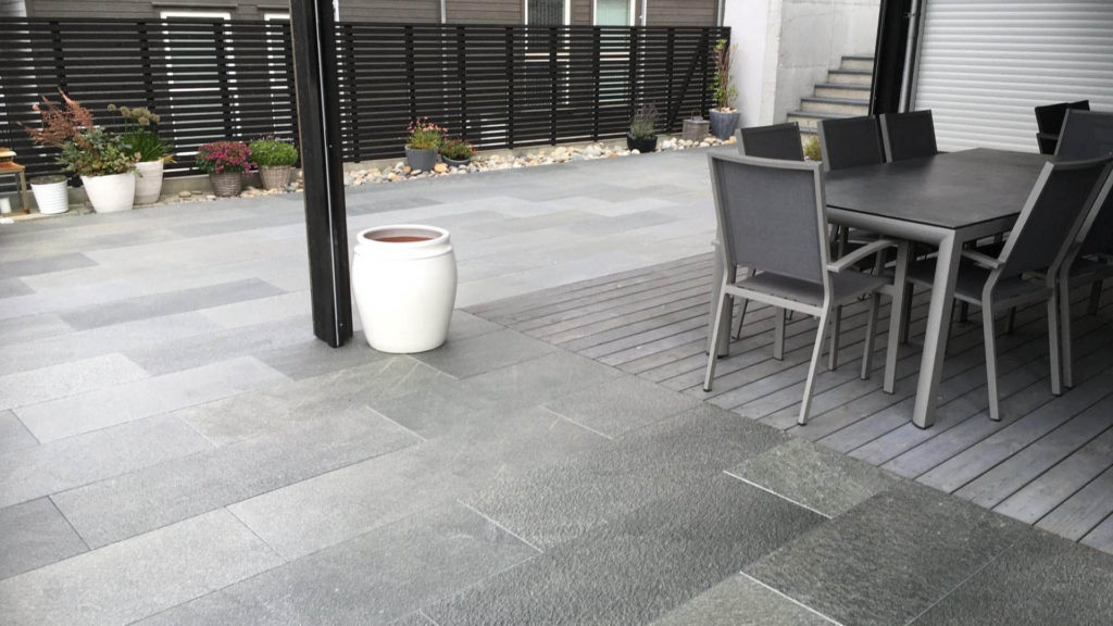 A large terrace with a dining area and with gray slate tiles from Offerdal. A bed of decorative stone runs along the edge.