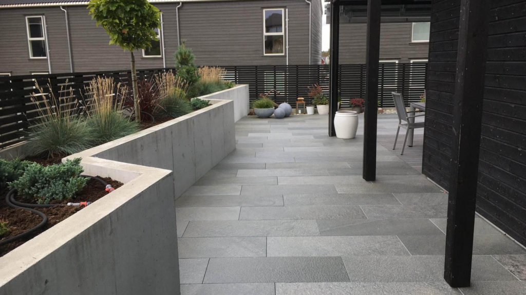 A large terrace with gray slate tiles from Offerdal. A flower bed with high concrete walls runs along one side.