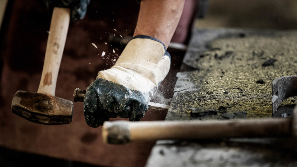 A stonemason works on a block of Offerdal slate, splitting the block with a hammer and chisel into thin slate slabs