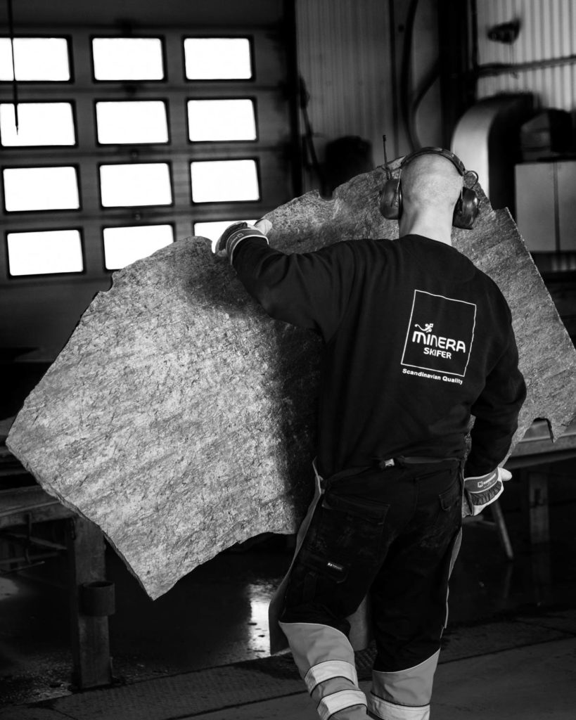 En stenhuggare bär en stor skifferplatta av svart skiffer från Otta inne i produktionshallen.