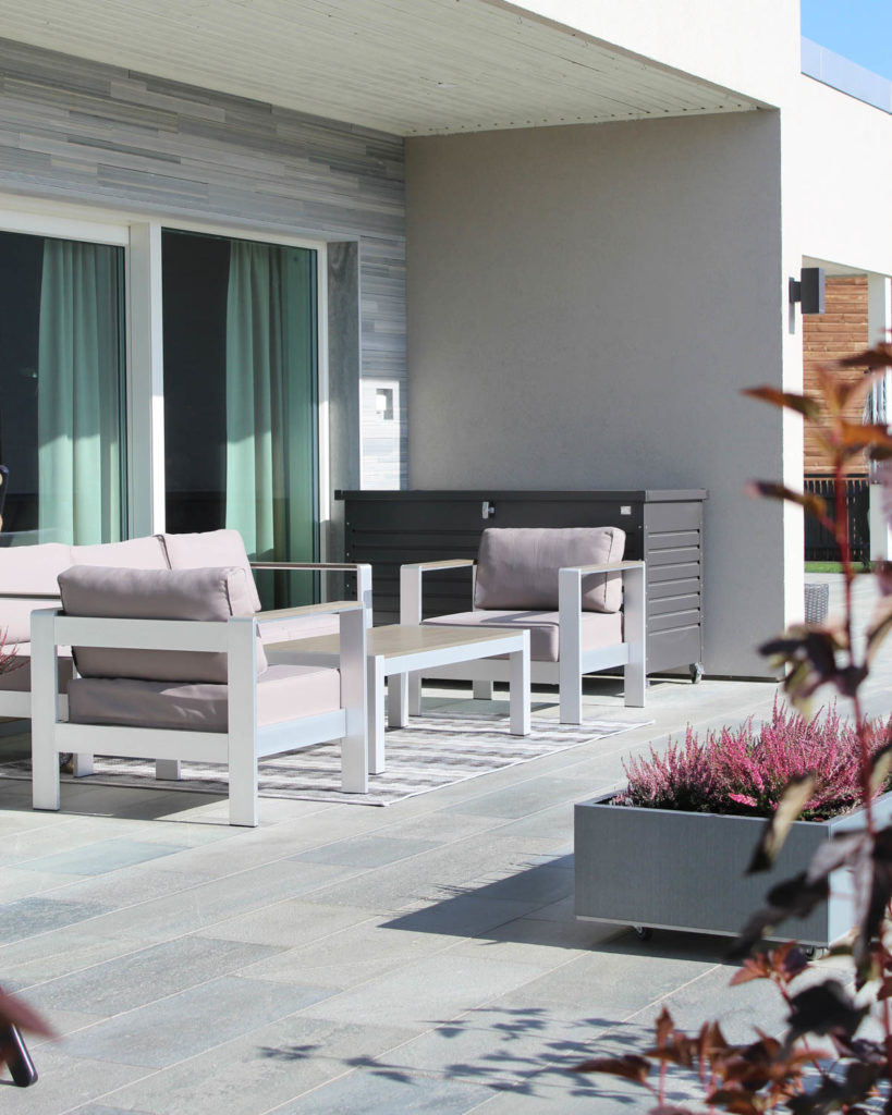 En terrasse med lyse Oppdal skiferflis . Den er møblert med lyse hagemøbler.
