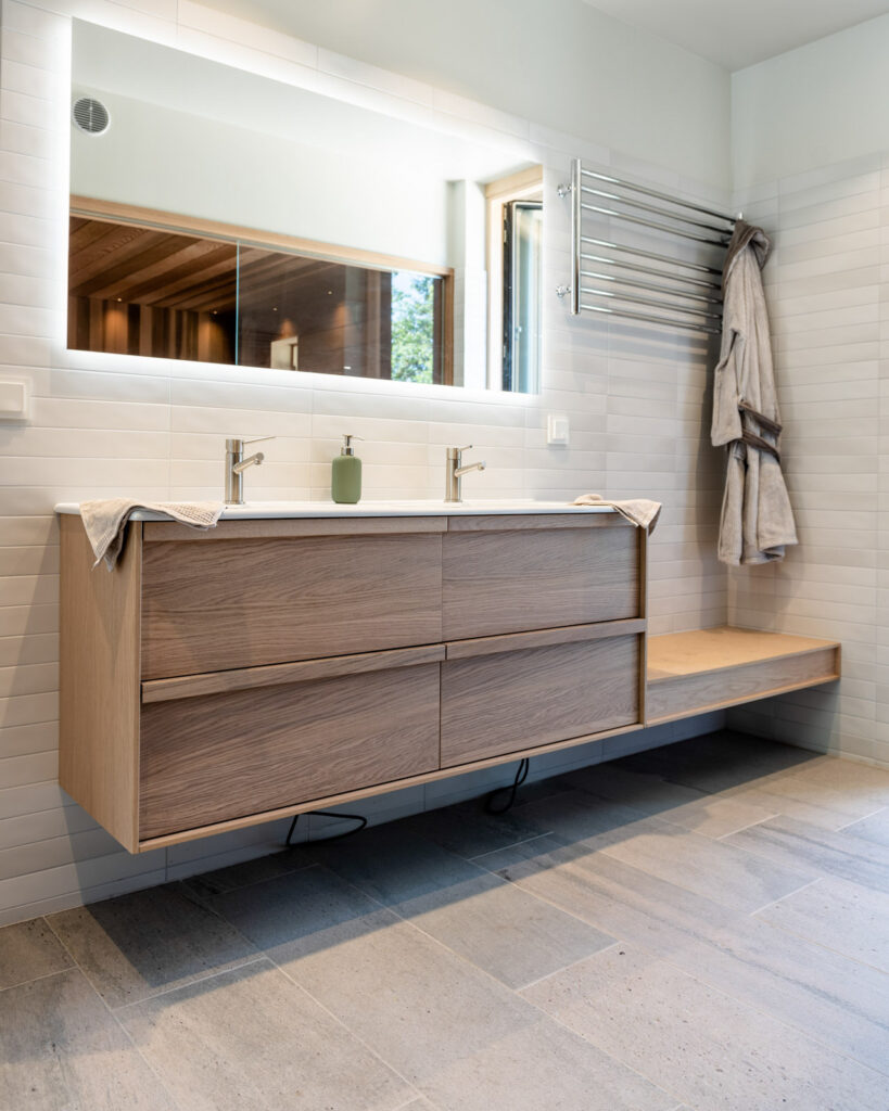 Et bad med lys grå skiferflis på gulv, et speil og badeinnredning i eik