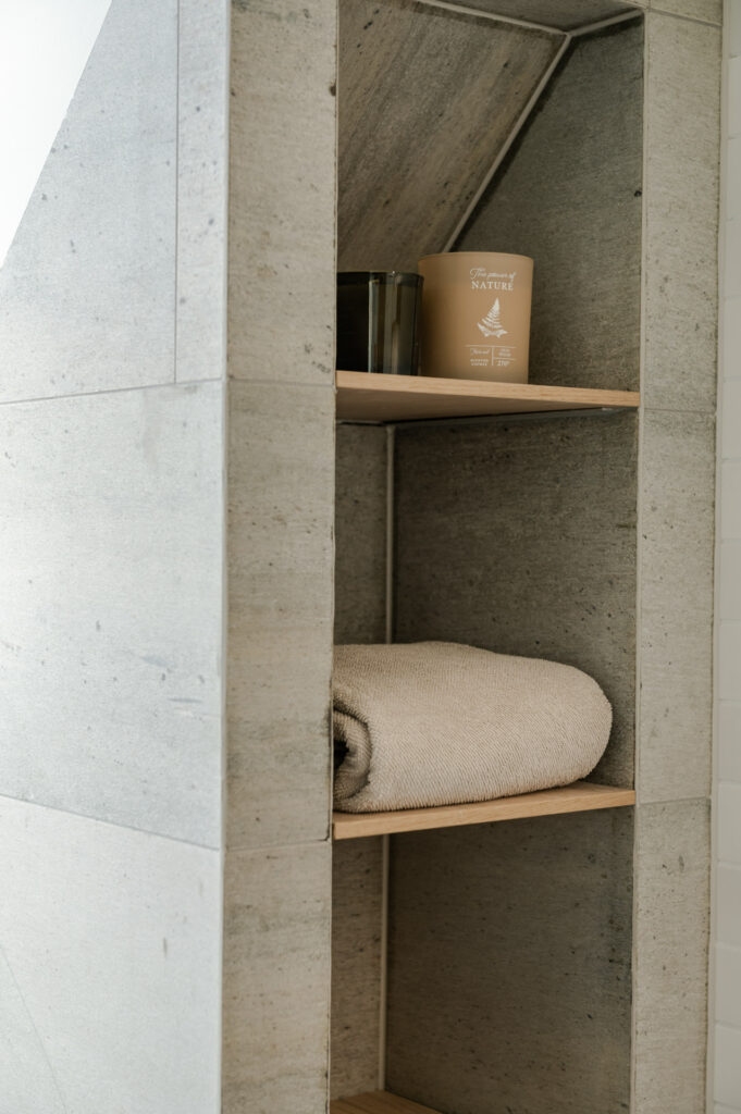 Detail from a bathroom with slate tiles on the walls and oak shelves.