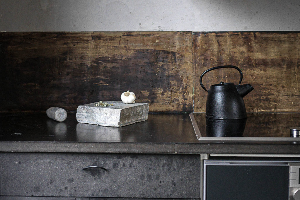 A kitchen with a light gray slate slab reused as a mortar for the clock and garlic.