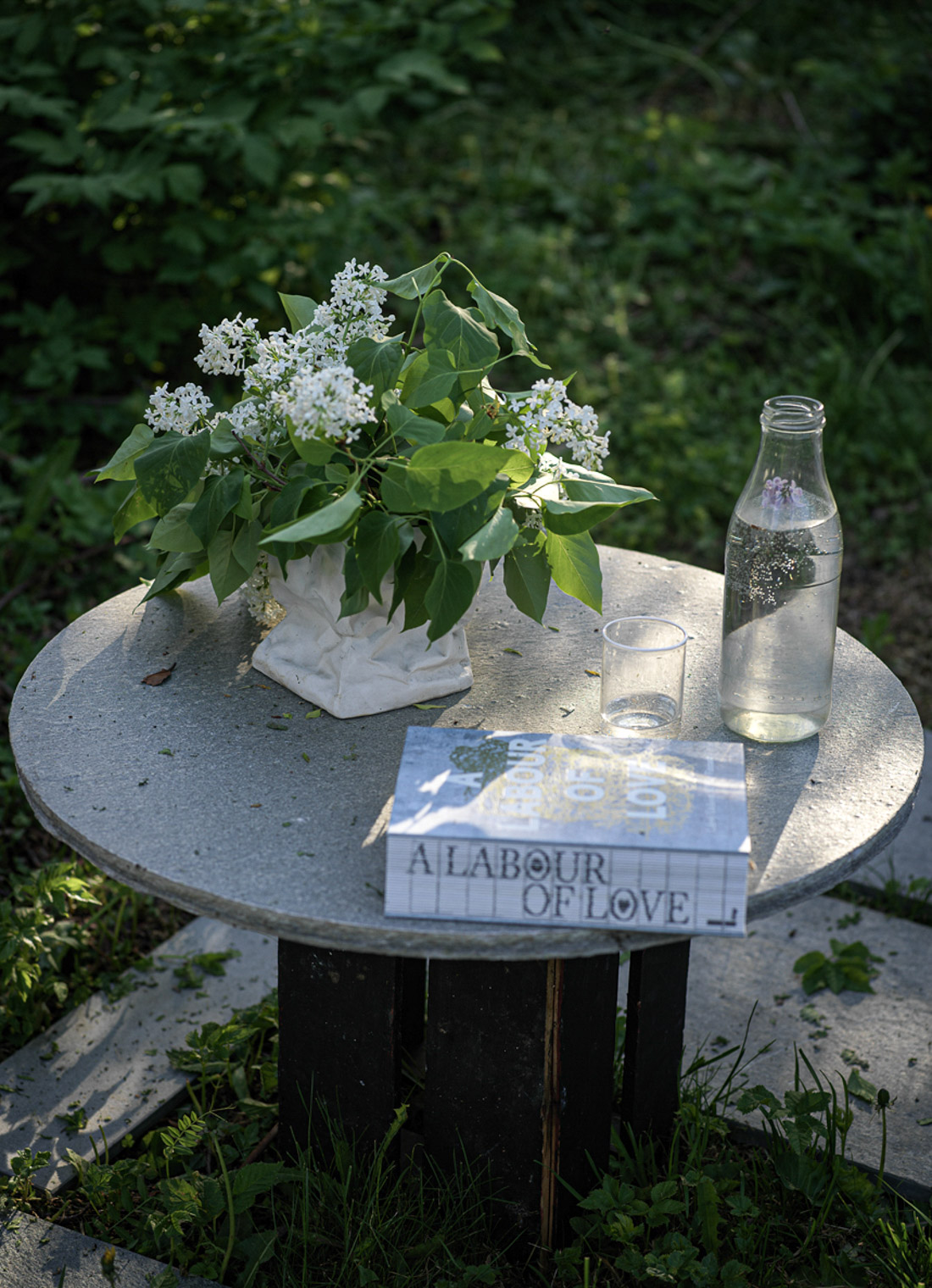 Et rundt steinbord av Oppdalskifer. På hagebordet sin skiferplate står en plante, et glass og en bok.