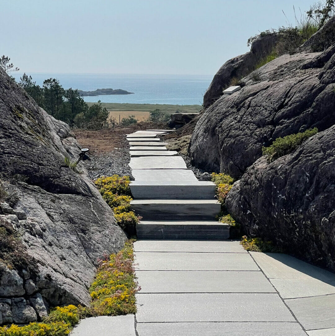 View from a patio covered with slate slabs. A slate staircase and stepping stones lead the way down to the sea.