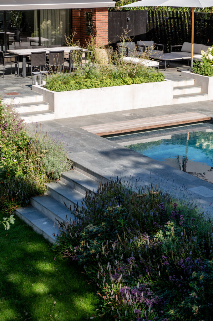 En hage og terrasse belagt med skiferflis. Fra baddenget går en trapp ned til hagen.