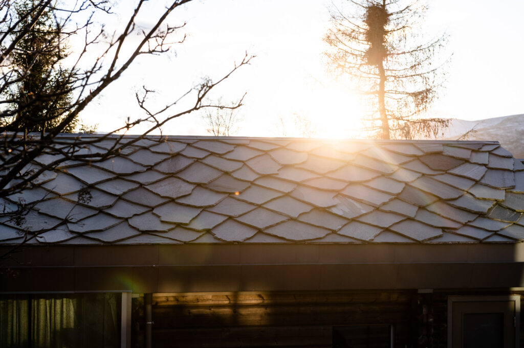 Ett modernt korsvirkeshus med skiffertak i oregelbunden skiffer. Solen tittar fram över taket.