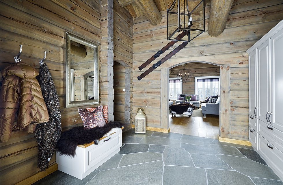 An entrance hall in a log cabin with light gray quarry slate on the floor. A pair of old skis hang on the wall.