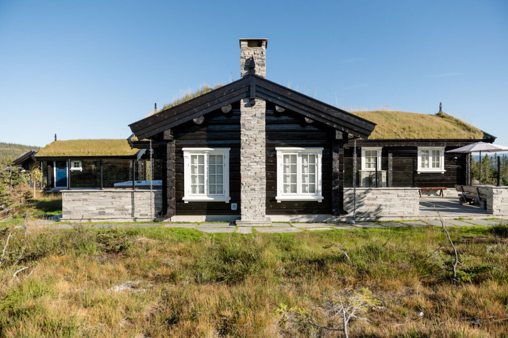 A dark log cabin with walls and chimney in dry stone made of light Oppdal slate. Slate tiles are used on the terrace.